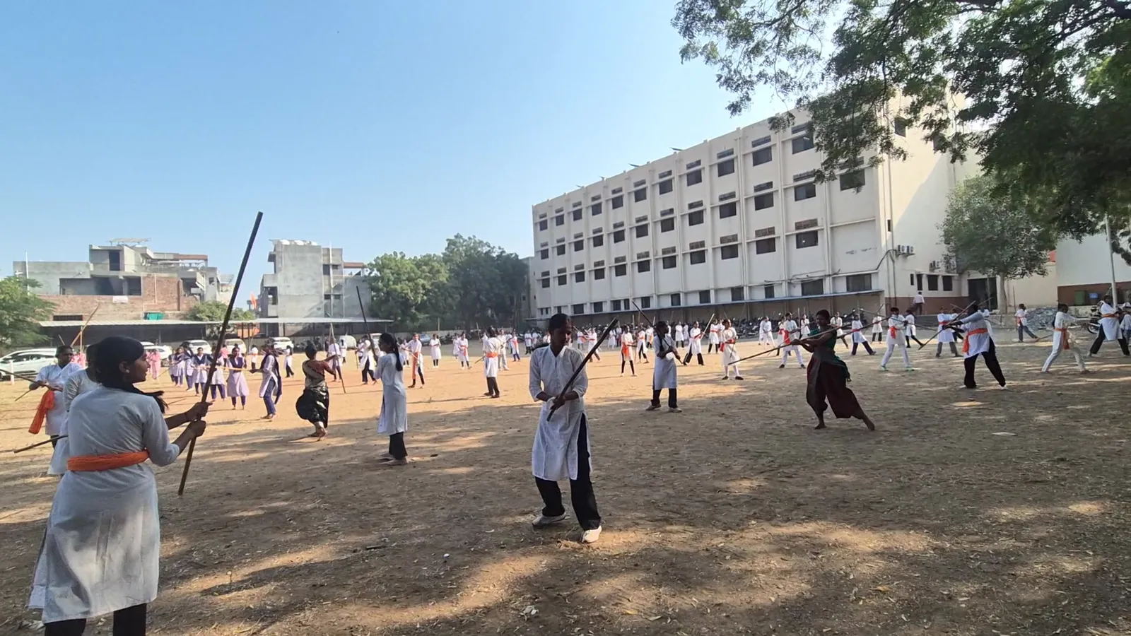 Girl mid swing while the whole ground practises Lathi Kathi at New Arts College, Shevgaon